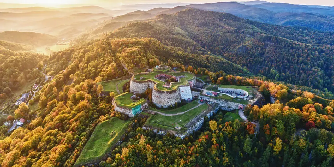 Twierdza Srebrna Góra otoczona jesiennym lasem, w świetle zachodzącego słońca.