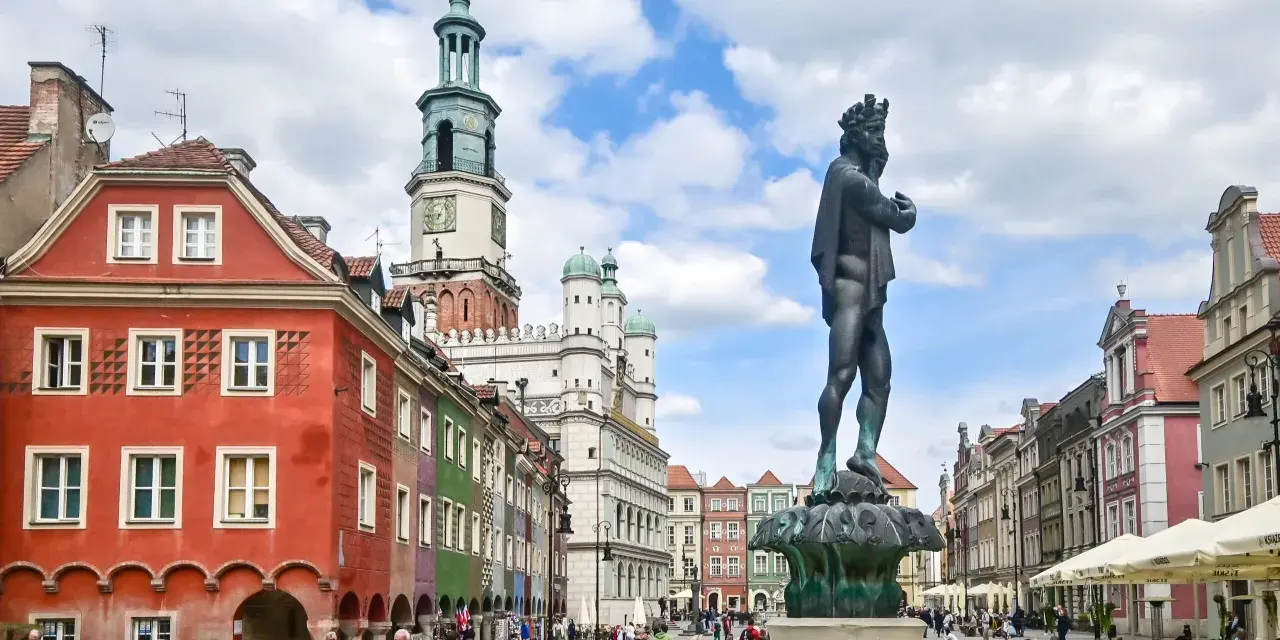 Pomnik króla na Rynku w Poznaniu, w tle kolorowe kamienice i ratusz.