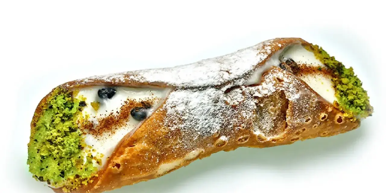 Sycylijski cannolo z kremem, pistacjami i borówkami, posypany cukrem pudrem.