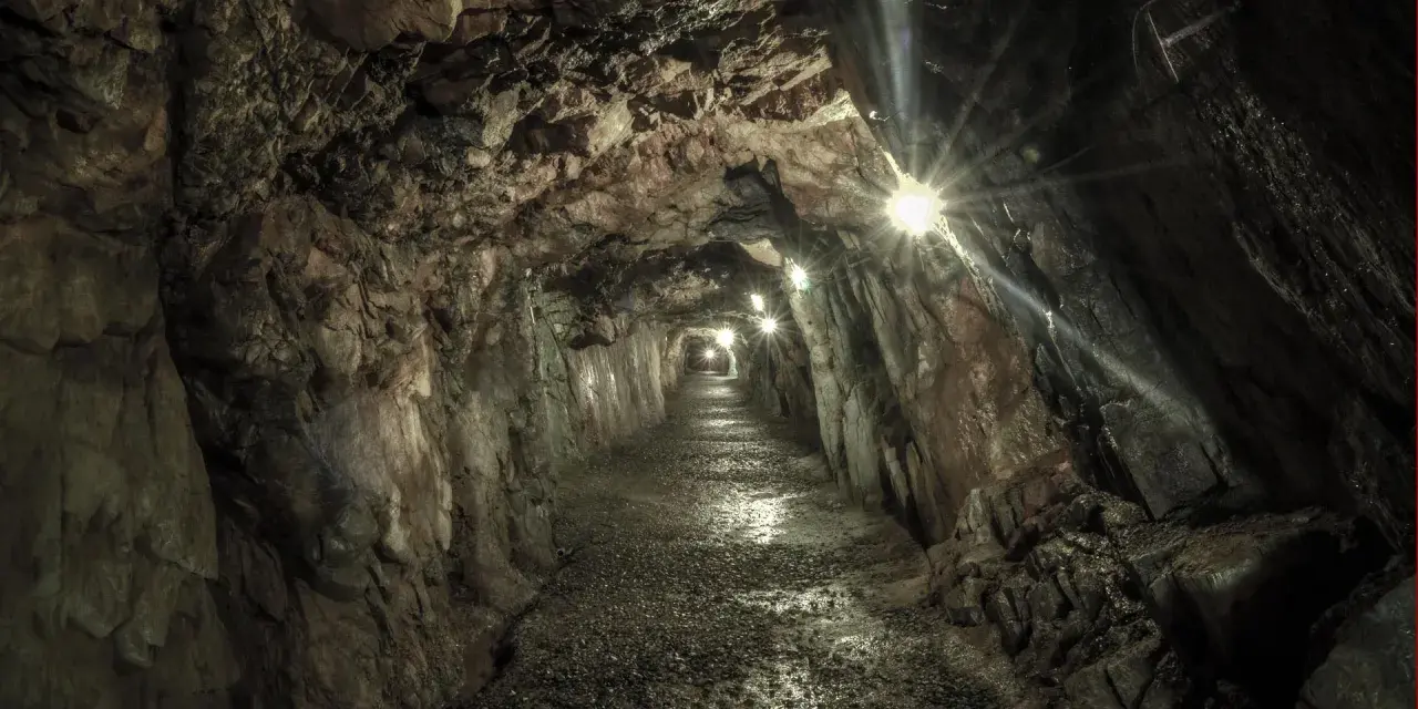Wydrążony tunel skalny z oświetleniem, kamienista ścieżka.
