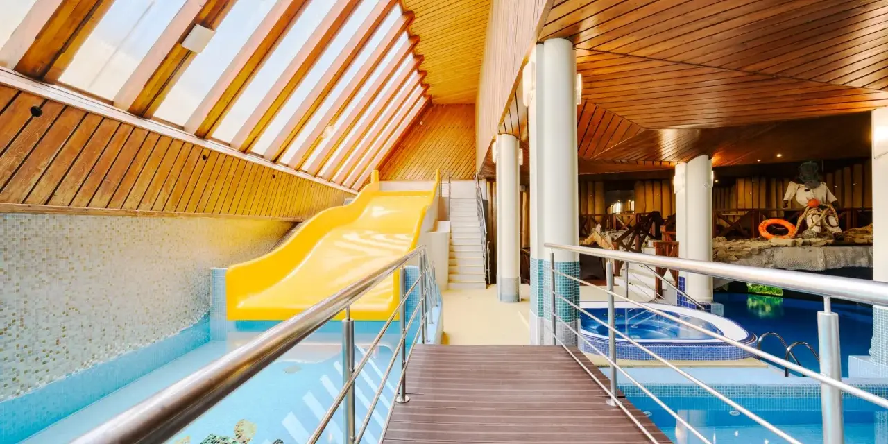 Wnętrze hotelowe z basenem, zjeżdżalnią i jacuzzi, drewniany sufit i ściany.