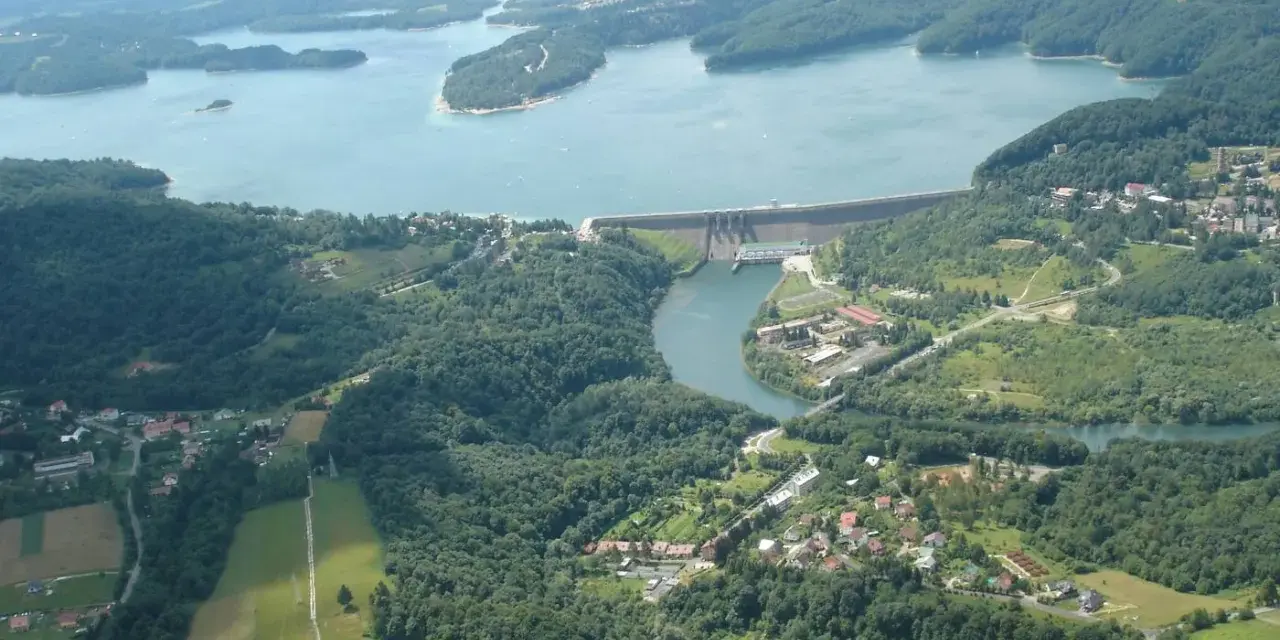 Widok z lotu ptaka na zalesione wzgórza, jezioro i zaporę wodną.