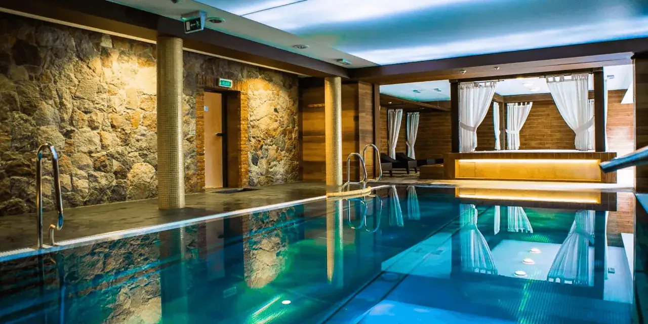 Basen w hotelu SPA z kamienną ścianą i drewnianymi elementami, z zasłonami w tle.