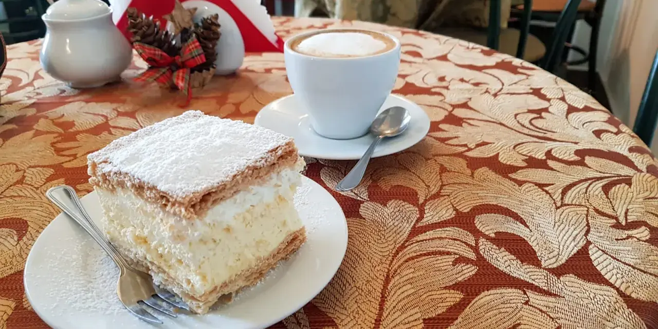 Kremówka posypana cukrem pudrem i filiżanka kawy na stoliku.