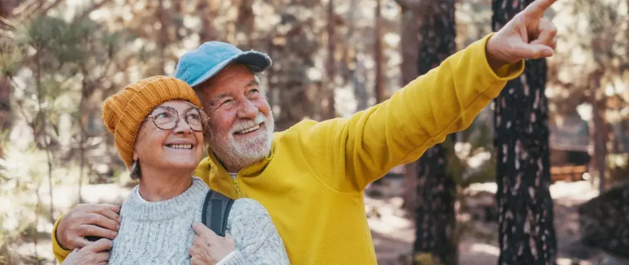 Uśmiechnięta para seniorów w górach, mężczyzna wskazuje palcem.