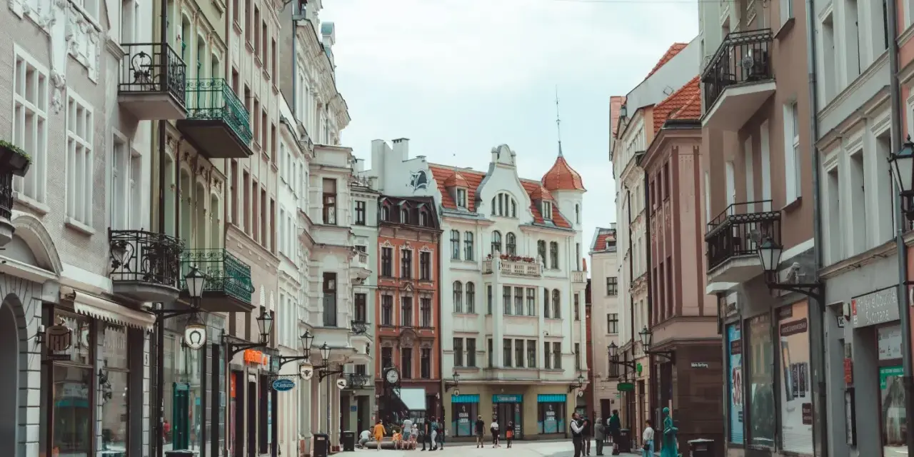 Ulica z kolorowymi kamienicami i ludźmi spacerującymi po bruku.