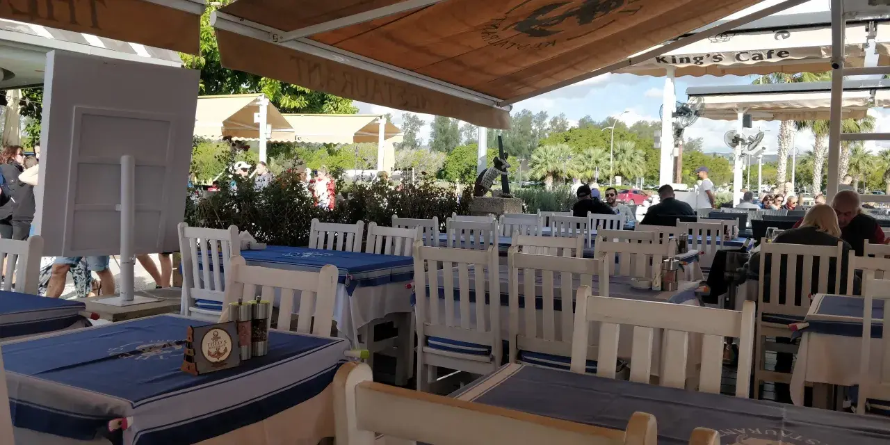 Stoliki w restauracji z niebiesko-białymi obrusami i białymi krzesłami, pod markizą.