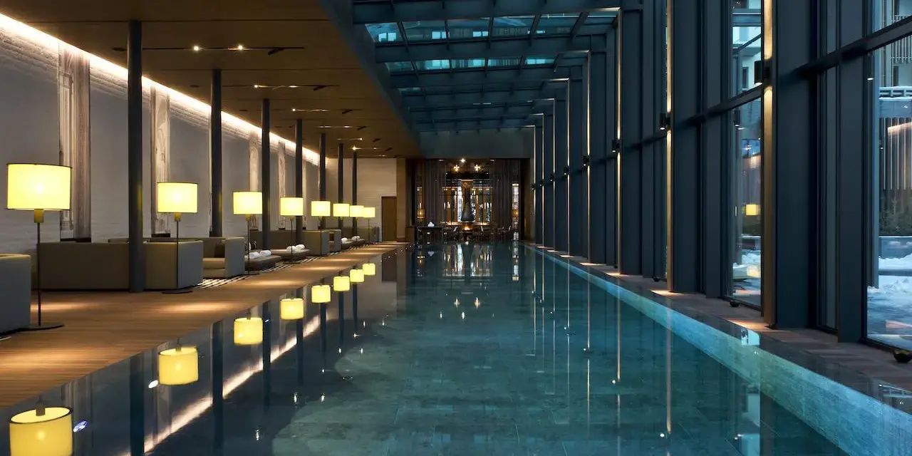 Nowoczesny basen hotelowy z przeszklonym dachem i oświetleniem, otoczony strefą relaksu.