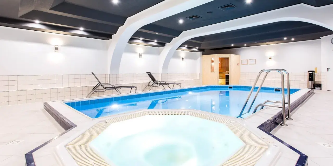 Wnętrze hotelowe z basenem, jacuzzi, sauną i leżakami.