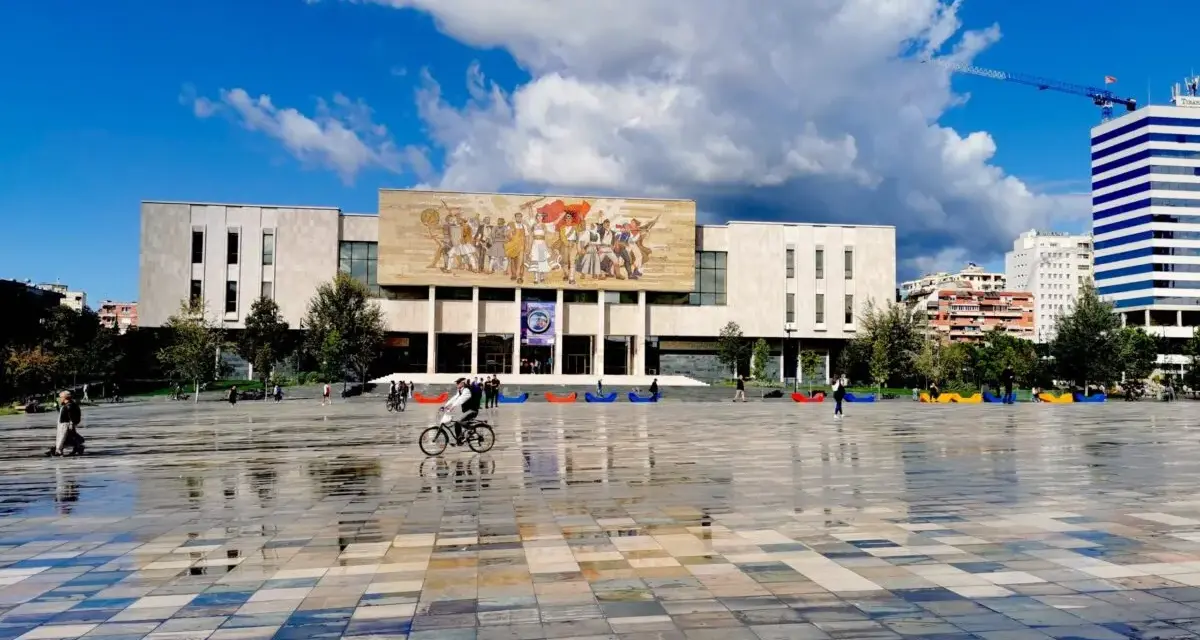 Plac w Tiranie z budynkiem Narodowego Muzeum Historii i kolorowymi pufami.