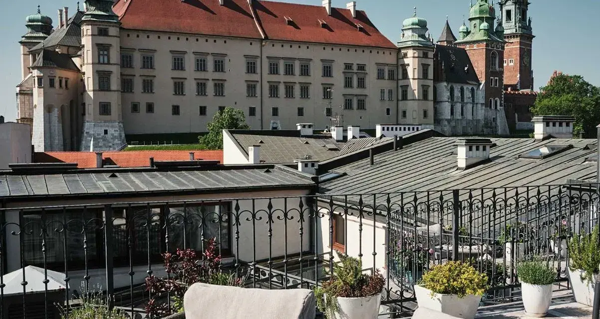 Widok z tarasu na Wawel, z meblami wypoczynkowymi i roślinami w donicach.