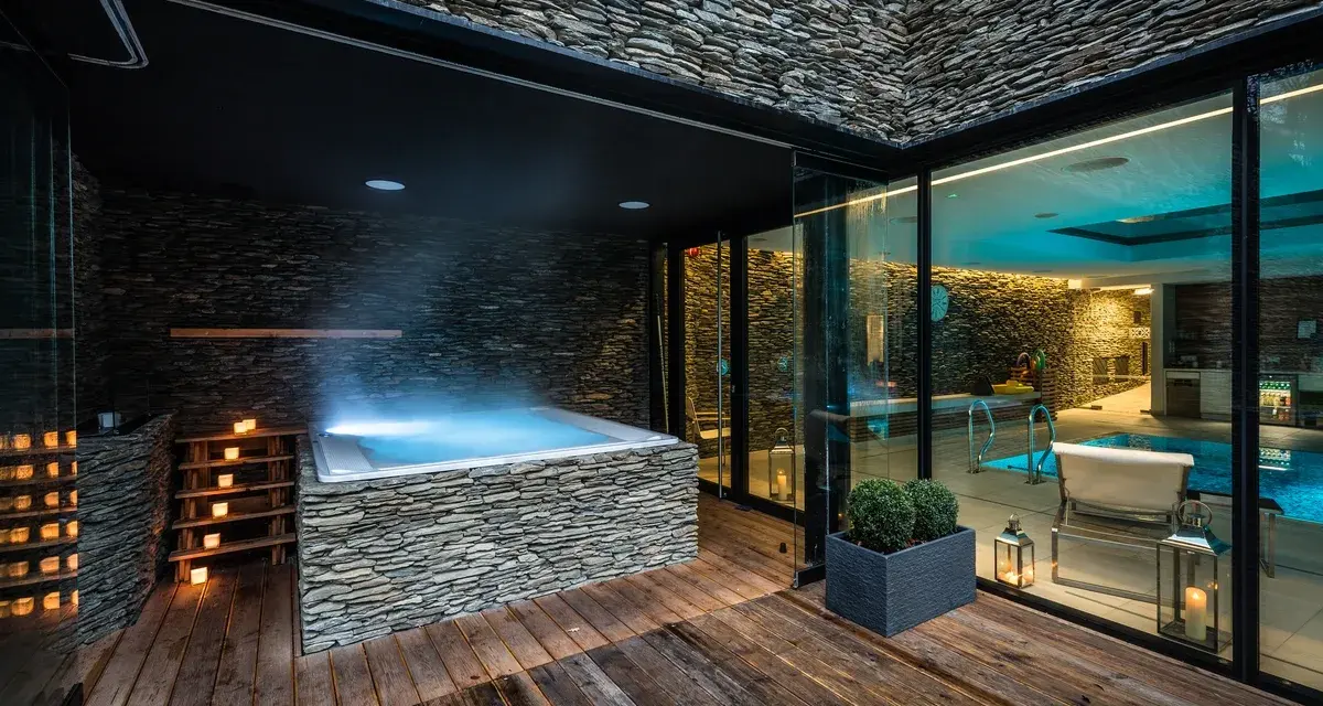 Nowoczesne jacuzzi z kamienną okładziną i oświetleniem, obok basenu.