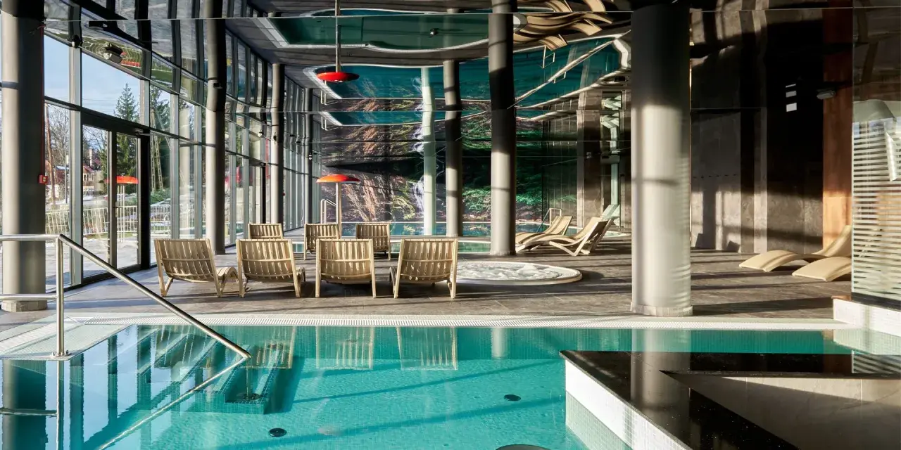 Basen z turkusową wodą i leżakami w nowoczesnym hotelowym spa.