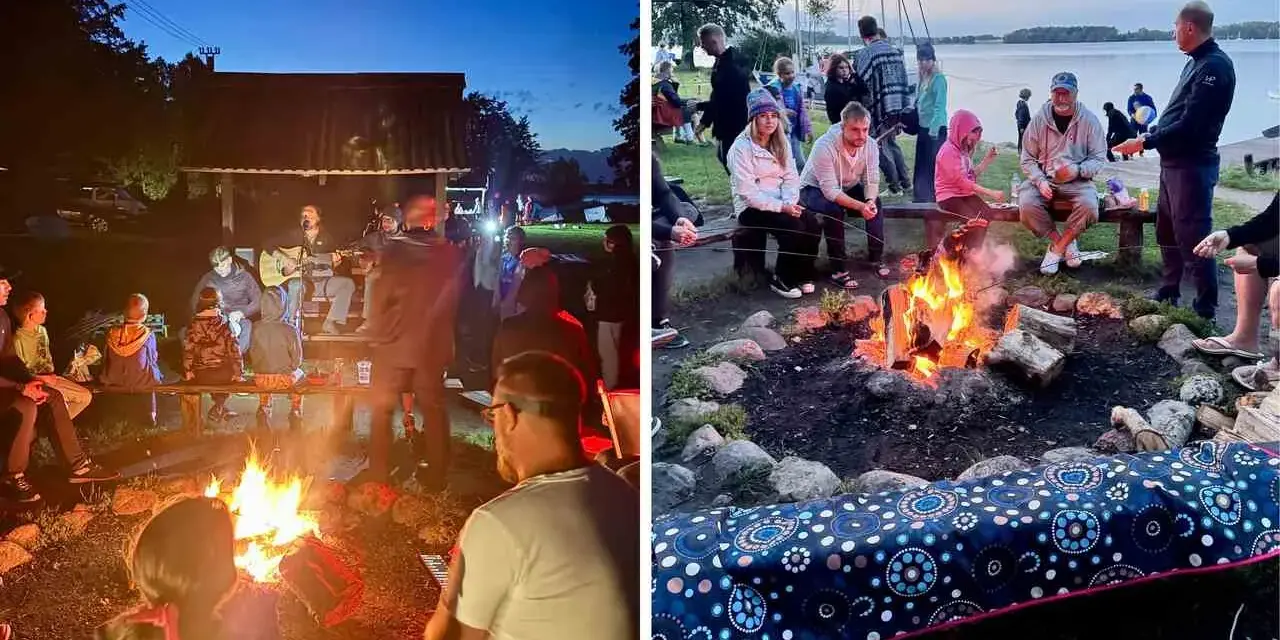 Grupa ludzi siedzi przy ognisku, niektórzy grają na gitarze, inni rozmawiają.