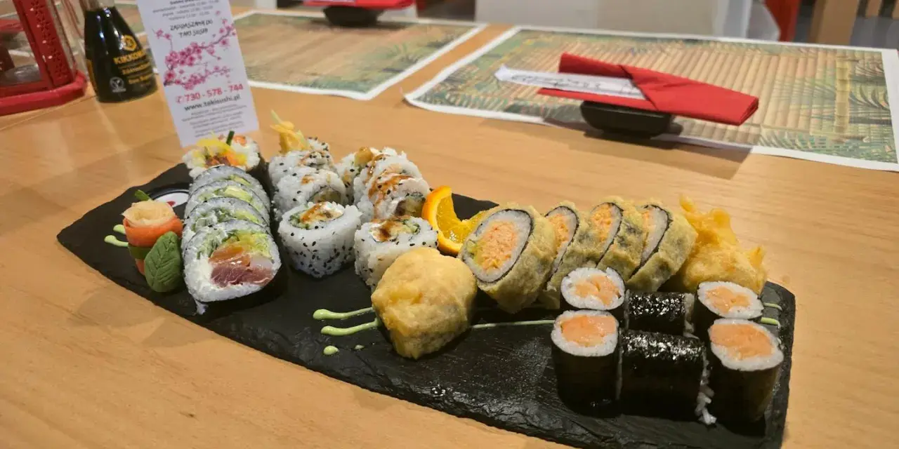 Talerz sushi z różnymi rolkami, w tym smażonymi i z łososiem, na czarnej desce.