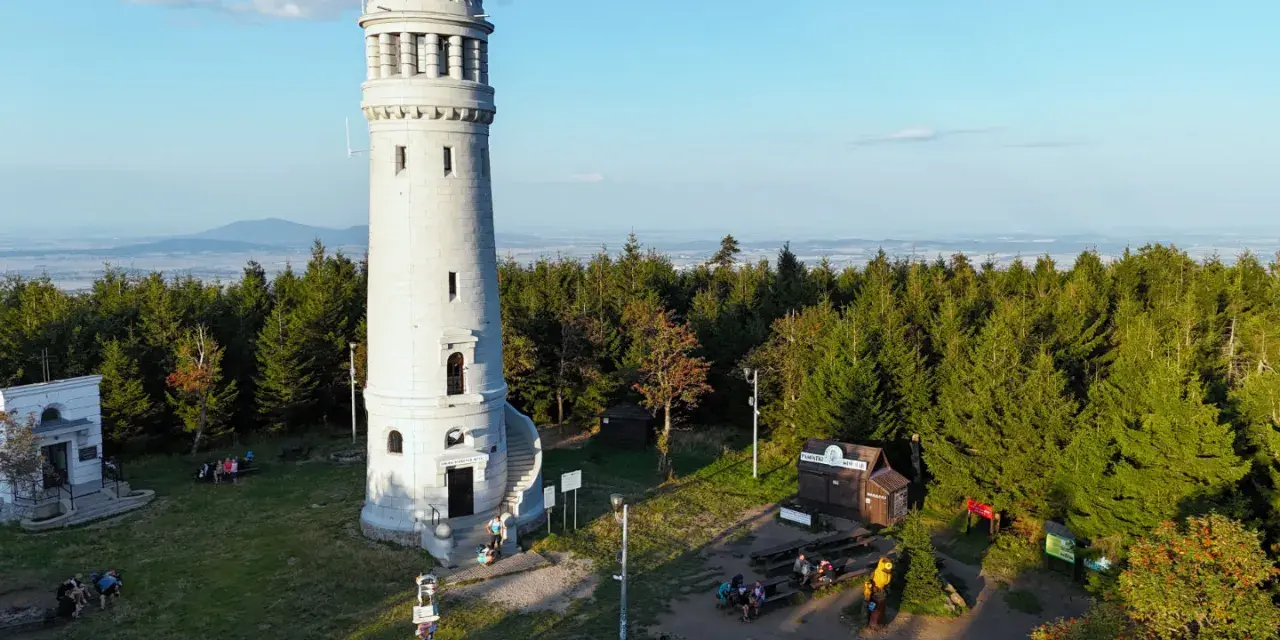 Kamienna wieża widokowa na szczycie góry otoczona lasem, z widokiem na krajobraz.