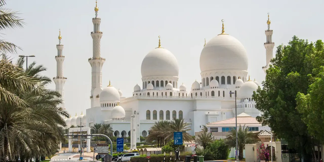 Wielki Meczet Szejka Zajida w Abu Zabi z minaretami i kopułami, otoczony palmami.
