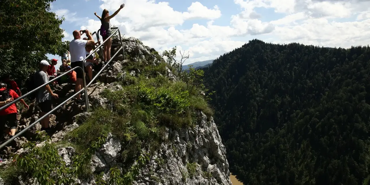 Grupa turystów na skalistym szczycie z widokiem na Pieniny i Dunajec.