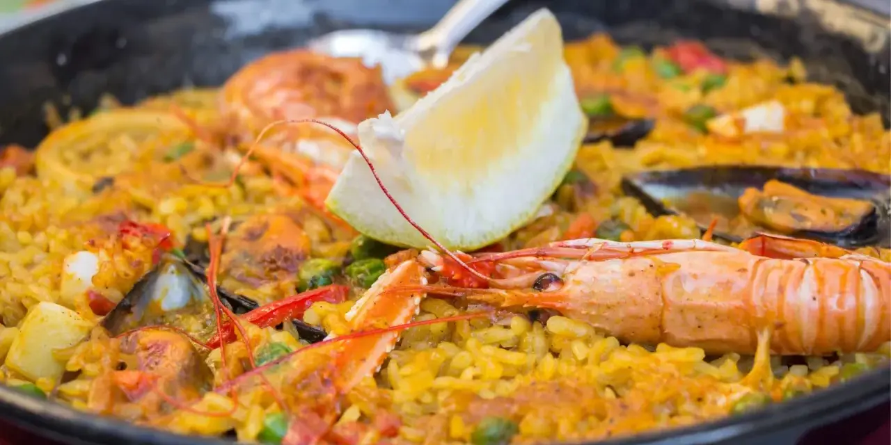 Paella z owocami morza i cytryną w czarnej patelni.