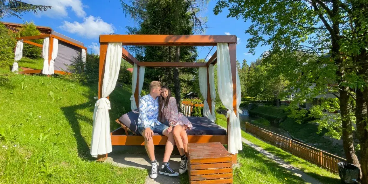 Para siedząca na łóżku pod baldachimem w otoczeniu zieleni.