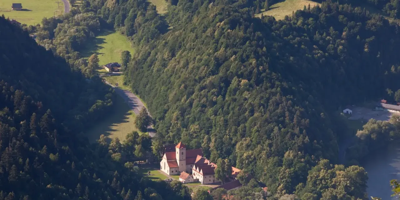 Widok z lotu ptaka na Czerwony Klasztor otoczony zielonymi wzgórzami i lasami.