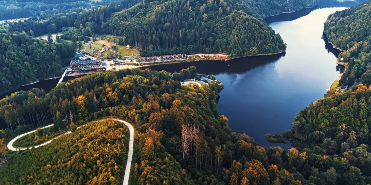 Widok z lotu ptaka na jezioro Bystrzyckie otoczone lasami, z krętą drogą i zabudowaniami.