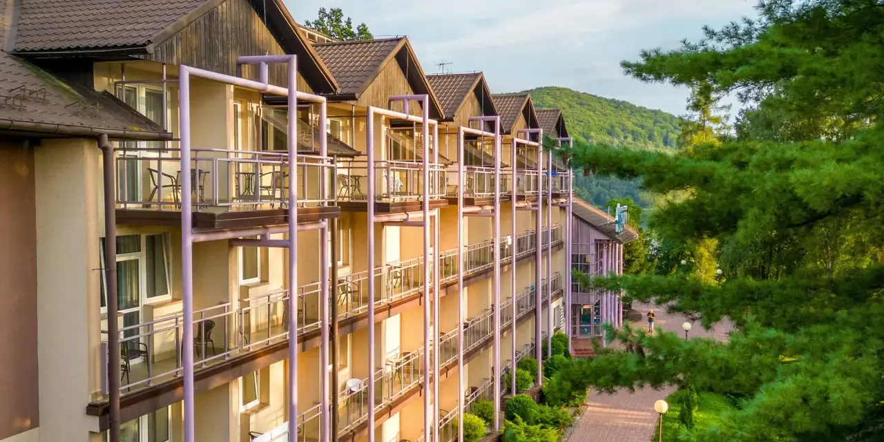 Hotel z balkonami w otoczeniu zieleni i gór.