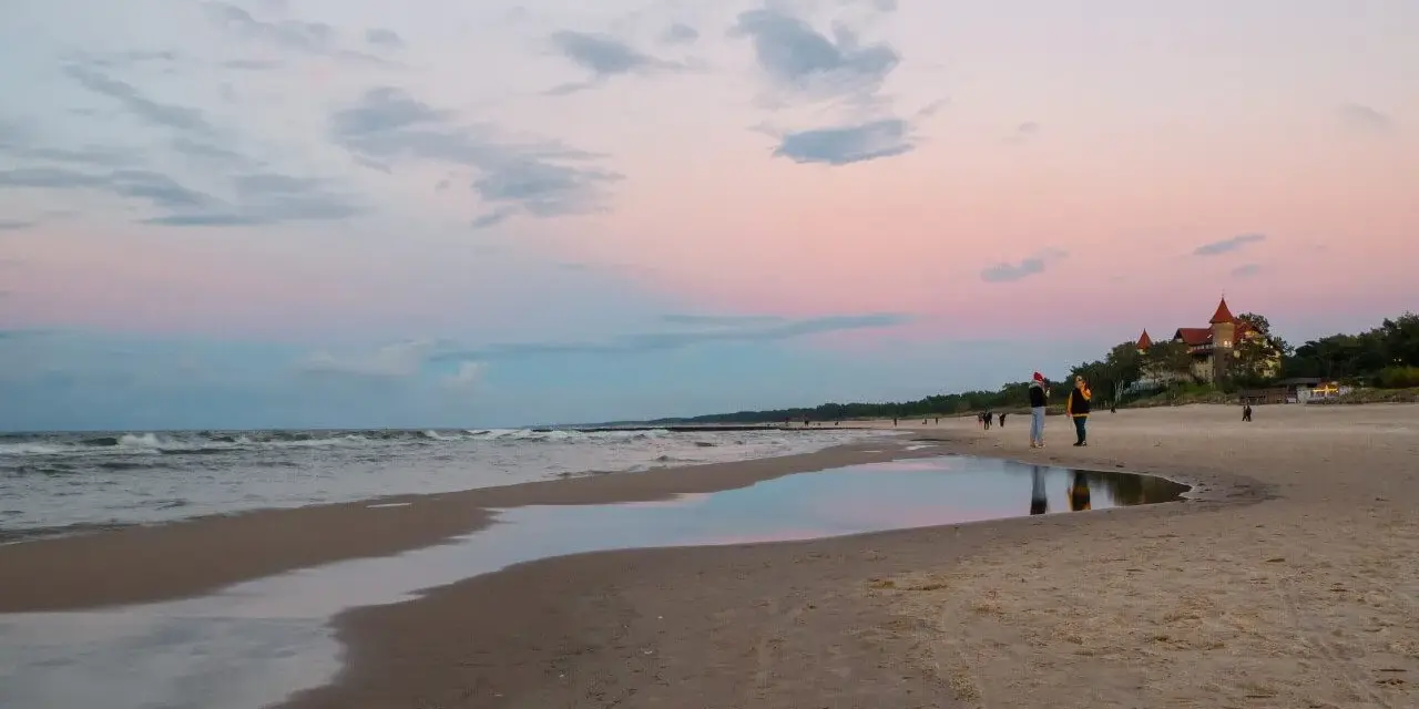 Plaża w Łebie o zachodzie słońca z widokiem na morze i budynek z czerwonym dachem.