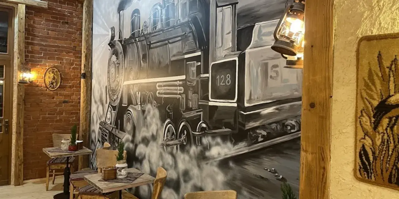 Wnętrze restauracji z muralem przedstawiającym lokomotywę i stoliki.