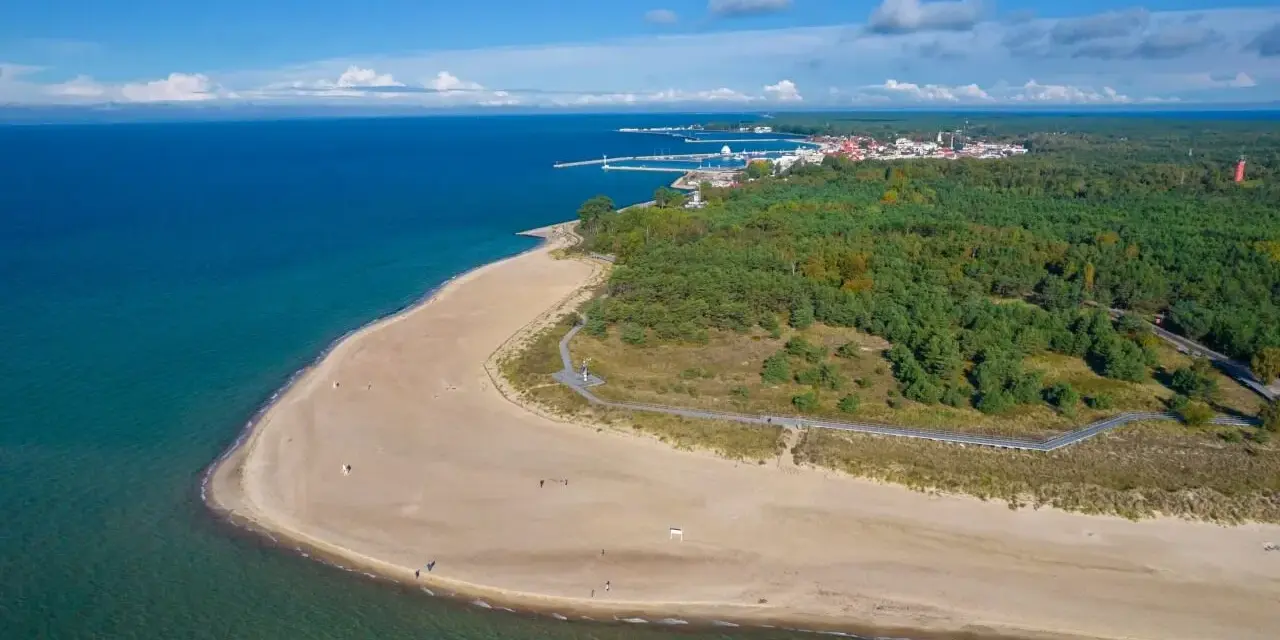 Widok z lotu ptaka na piaszczystą plażę, las i miasteczko na Półwyspie Helskim.
