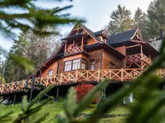 Drewniany góralski pensjonat z tarasem i balustradą, otoczony drzewami.