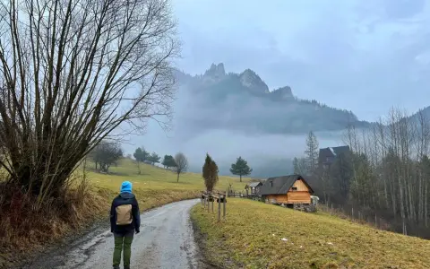 Osoba w niebieskiej czapce idzie drogą w Pieninach, w tle góry i drewniane chatki.
