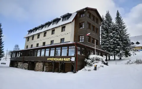 Hotel w Zieleńcu zimą, z widoczną wypożyczalnią nart i stosem drewna.