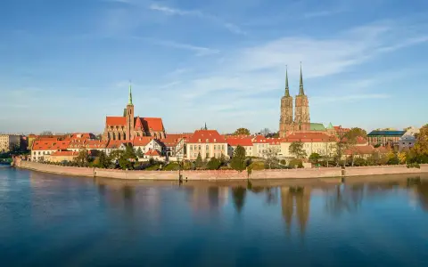 Widok na Ostrów Tumski we Wrocławiu z rzeką i odbiciem budynków w wodzie.