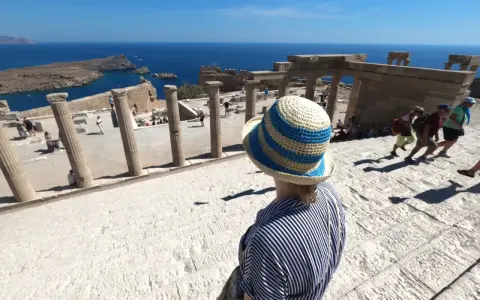 Kobieta w kapeluszu na tle starożytnych ruin i morza.
