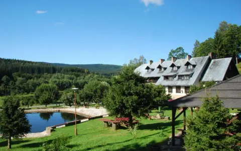 Budynek pensjonatu z kamiennym stawem i zielonym ogrodem w Górach Orlickich.