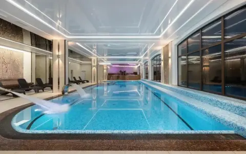 Nowoczesny basen w hotelu spa z wodospadem i leżakami.