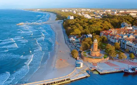 Widok z lotu ptaka na plażę, morze, latarnię morską i zabudowania Kołobrzegu.