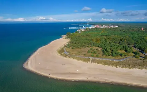Widok z lotu ptaka na piaszczystą plażę, turkusowe morze i zielony las z miasteczkiem w tle.