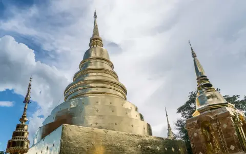 Złote stupy świątyni Wat Phra Singh w Chiang Mai na tle błękitnego nieba z chmurami.