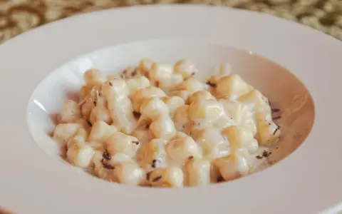 Kluski gnocchi w kremowym sosie z tartą truflą na białym talerzu.