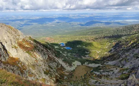 Widok z góry na skaliste zbocze, dolinę z dwoma stawami i lasy w tle.