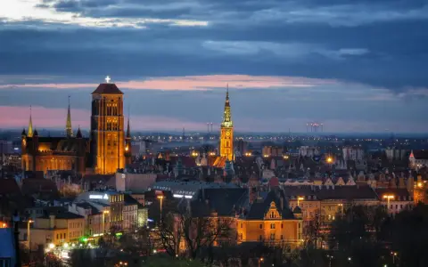 Widok na oświetlone zabytkowe centrum Gdańska o zmierzchu, z dominującą Bazyliką Mariacką i Ratuszem Głównego Miasta.