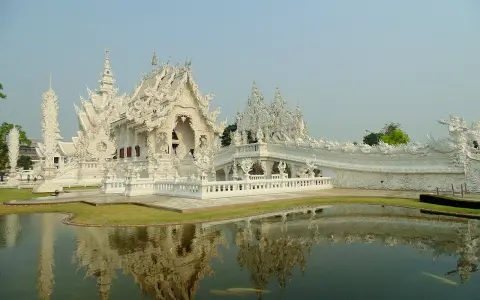 Biała świątynia Wat Rong Khun w Tajlandii z odbiciem w stawie.