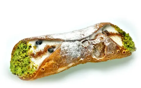 Sycylijski cannolo z kremem, pistacjami i borówkami, posypany cukrem pudrem.