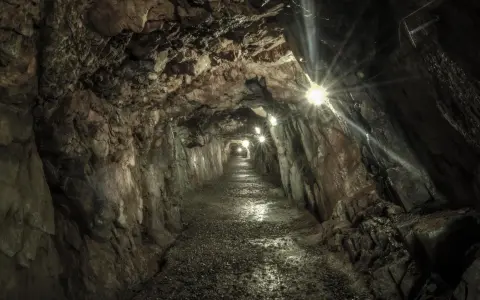 Wydrążony tunel skalny z oświetleniem, kamienista ścieżka.