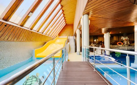 Wnętrze hotelowe z basenem, zjeżdżalnią i jacuzzi, drewniany sufit i ściany.