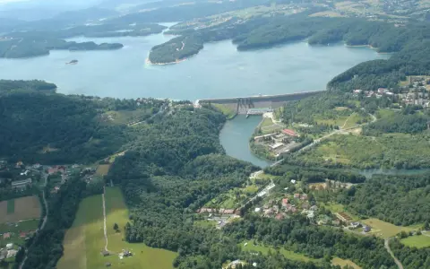 Widok z lotu ptaka na zalesione wzgórza, jezioro i zaporę wodną.
