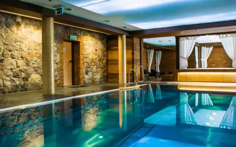 Basen w hotelu SPA z kamienną ścianą i drewnianymi elementami, z zasłonami w tle.