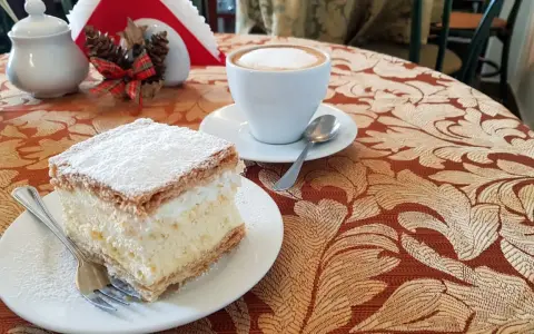 Kremówka posypana cukrem pudrem i filiżanka kawy na stoliku.